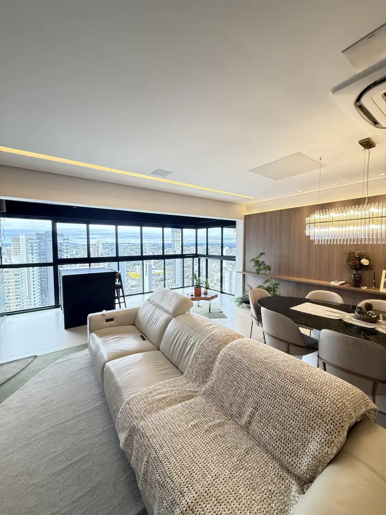 Antes: a sala de estar com a janela panorâmica sem cortina, com a vista da cidade aberta e a luz batendo direto no sofá.