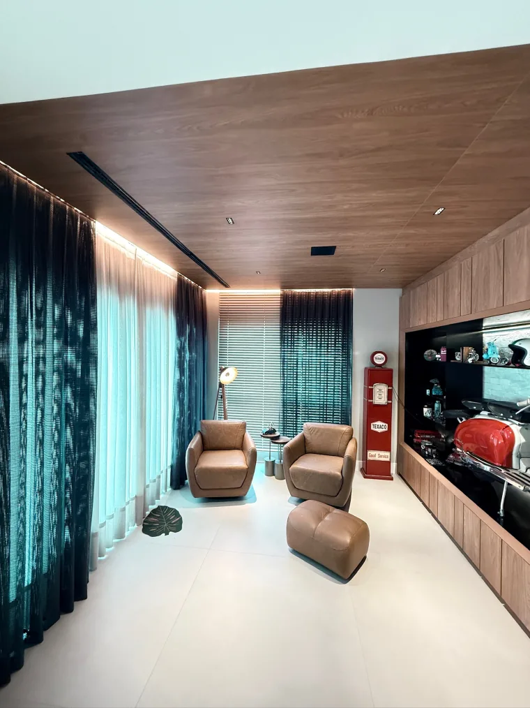 Sala residencial com cortina escura e voil numa janela e persiana horizontal de madeira na outra, no mesmo ambiente.