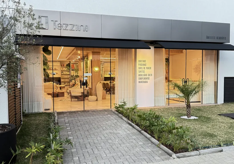 Fachada do showroom da Tezzini, com o letreiro da marca sobre o toldo preto e a vitrine de vidro mostrando os ambientes montados por dentro.