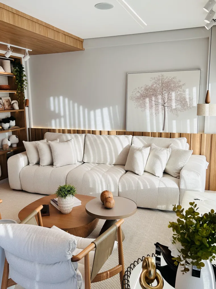 Ambiente montado no showroom, com sofá de bouclê branco, duas mesas de centro redondas e estante de madeira com peças de decoração.