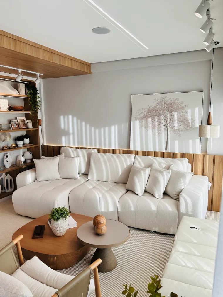 Sofá de bouclê branco em L com almofadas, mesas de centro e estante de madeira com peças de decoração e livros.