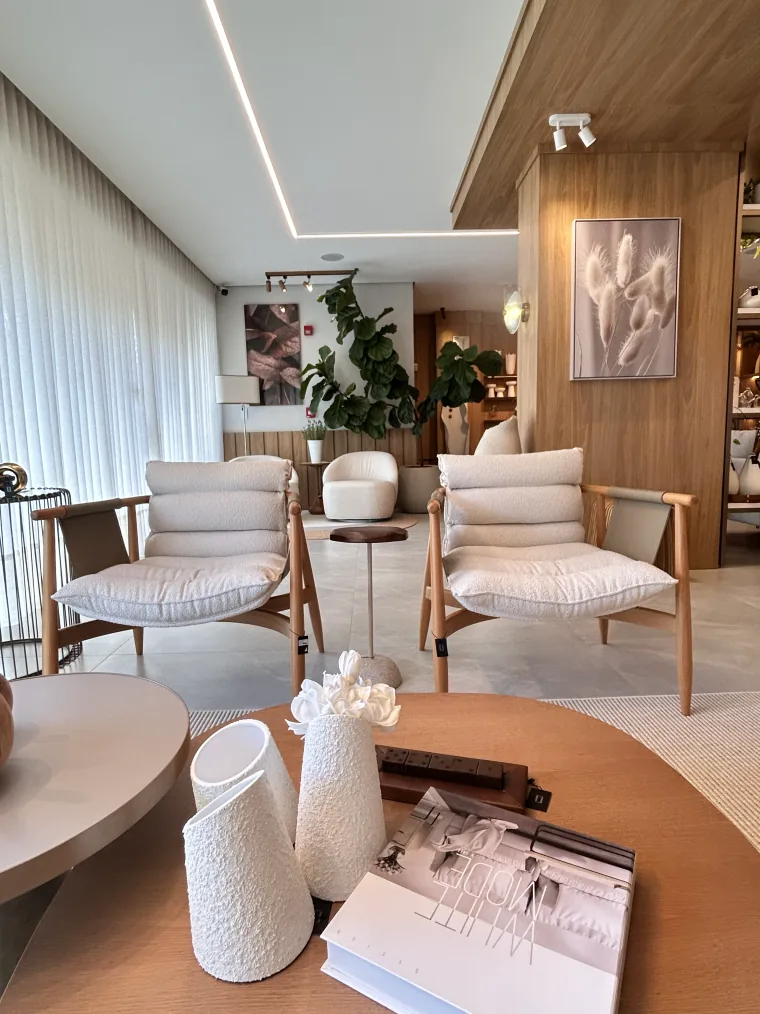 Duas poltronas de bouclê claro com estrutura de madeira, mesa lateral e quadros, num ambiente montado do showroom.